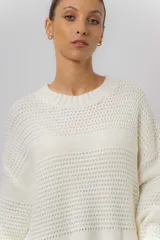 Buzo tipo sweater de punto color blanco, con diseño de trenzas verticales, cuello redondo, mangas largas y tajos laterales. Presenta un corte oversize y largo extendido.