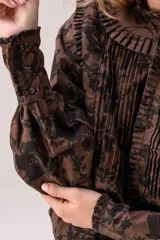 Camisa de manga larga marrón con estampado floral en negro, cuello mao con volados, pliegues frontales y puños ajustados.