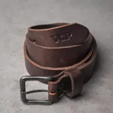 Cintur&oacute;n de cuero color chocolate con hebilla met&aacute;lica rectangular envejecida y logo grabado en la punta.