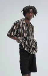 Camisa de manga corta tejida en punto abierto (símil crochet), con calce oversize. Presenta un patrón geométrico en tonos negro, marrón y blanco.