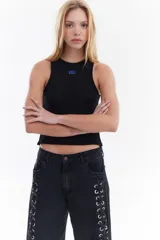 Top musculosa blanco de canalé con cuello redondo, corte ajustado y detalle de botones a presión en el lateral.