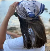 Pañuelo de cabeza tipo bandana, de color blanco con estampado lineal en azul marino que representa figuras arquitectónicas y detalles geométricos.