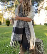 Bufanda tipo chal con diseño a rayas horizontales en tonos blanco, gris y negro, con flecos en los extremos.