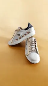Championes de cuero color blanco y marfil, con detalles pintados a mano por Carolina De Cunto, apliques en tono dorado, talón negro y suela de goma.