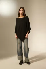 Poncho negro de tejido de punto con diseño asimétrico y detalle de pequeñas aplicaciones brillantes distribuidas por toda la superficie. Presenta un borde acanalado en el ruedo.