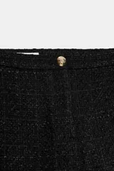 Short de tiro alto confeccionado en tweed negro, con cierre frontal y botón dorado decorativo.