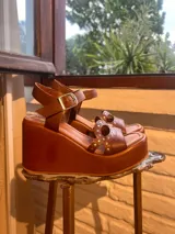 Sandalias de plataforma corrida color marrón, con tira en el talón con hebilla metálica y tiras delanteras adornadas con tachas y recortes circulares.