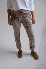 Pantalón de corte recto y ajuste holgado, color visón con estampado floral en tonos tierra. Presenta cintura elástica con cordón ajustable y ruedos doblados.