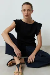 Top de tejido canalé color negro, con cuello redondo y mangas cortas con volados decorativos en los hombros.