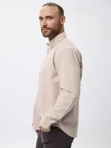 Camisa de manga larga en algodón tramado, con cuello clásico abotonado y cierre frontal con botones. Presenta un diseño liso con textura visible y un pequeño bordado en la pechera.