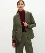 Blazer de sastrería color verde oliva, con corte oversized, solapas clásicas, cierre frontal de un botón y bolsillos con tapa. Cuenta con forro interno y textura sutil.