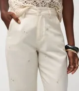 Pantalón de mujer color blanco roto, de corte recto y tiro alto, con un largo cropped y ligero ensanchamiento en el bajo. Presenta detalles bordados florales sutiles en la tela y bolsillos.