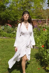 Vestido blanco de crepe con escote en V, mangas largas abullonadas con elástico en los puños, largo irregular, lazo para ajustar en la cintura y volado en el ruedo.