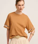 Blusa boxy de color tostado, corte holgado y cuello redondo, confeccionada en algodón con mangas cortas amplias que presentan detalles de entremedios ahuecados.