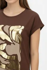 Remera de algodón blanca, de corte holgado, manga corta con vuelta y cuello redondo. Cuenta con un estampado frontal abstracto con trazos en tonos marrón y foil dorado.