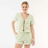 Pijama de dos piezas de cuadros vichy en tonos verde claro y blanco. Incluye una camisa de manga corta con escote en V y cierre frontal mediante lazos, y un short con cintura elástica y cordón ajustable. Ambas prendas cuentan con detalles de ondas bordadas en los bordes.