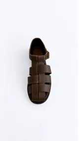 Sandalias cangrejeras de gamuza color marrón, con punta redonda, taco bajo, talonera cerrada y tira con hebilla metálica ajustable en el tobillo.