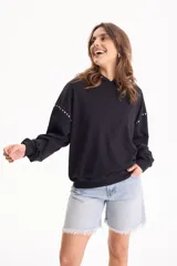 Buzo negro con capucha y detalle de tachas plateadas en las costuras de las mangas y escote.