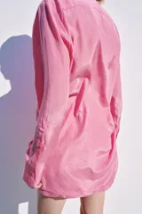 Blusa fluida de color rosado con cuello redondo ajustable mediante lazadas del mismo tejido, manga larga con puño y bajo asimétrico con aberturas laterales.