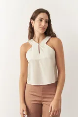 Top de lino color beige, sin mangas, con escote cruzado, cut out frontal y botón a tono.