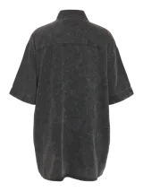 Vestido camisero corto de denim negro con lavado ácido, manga corta, cierre frontal con botones, dos bolsillos con solapa en el pecho y corte holgado.