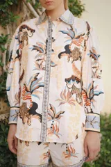 Camisa de popelina de algodón blanca con estampado tropical de tigres y palmeras en tonos neutros y azules, cuello camisero, mangas largas abullonadas con puños anchos y botonadura frontal oculta.