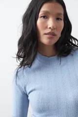Polera de tejido de punto con textura calada y diseño de líneas verticales acanaladas. Presenta cuello alto y mangas largas con puños delicados, de silueta entallada.