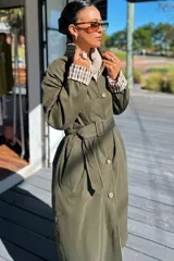 Trench reversible de corte largo, color verde militar con interior estampado a cuadros. Presenta cierre frontal con botones, cuello clásico y cinturón ajustable con hebilla a tono.