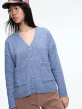 Cardigan de punto color beige con cierre frontal de botones, cuello en V y dos bolsillos delanteros. Presenta mangas largas con puños acanalados y un diseño de corte holgado.