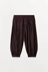 Pantalón de tiro bajo confeccionado en viscosa, con diseño abullonado y tejido plisado. Presenta detalles de apliques circulares en la cintura y terminaciones en los puños con tejido crochet a tono.
