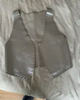 Chaleco de cuero negro con tachas plateadas en el borde.