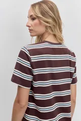 Remera de manga corta con cuello redondo, confeccionada en tejido de punto con diseño de rayas horizontales en tonos marrón, blanco y celeste. Presenta un pequeño parche circular rojo en el pecho.