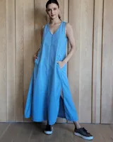 Vestido largo de denim azul, con escote en V, sin mangas, corte holgado, bolsillos laterales y aberturas en los costados de la falda.