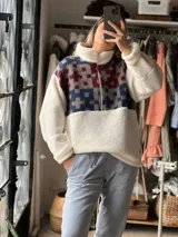 Buzo de corderito blanco con diseño de medio cierre frontal. Presenta un panel superior con estampado geométrico en tonos azul, gris y bordó, confeccionado con textiles vintage recuperados.