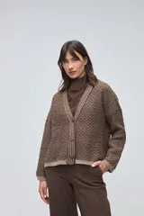 Cardigan de tejido de punto con textura, silueta boxy y cuello en V. Presenta cierre frontal con botones y detalles de terminación en contraste de color en los bordes.