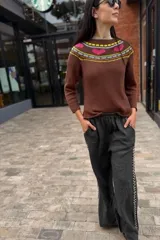 Sweater marrón de tejido de punto con cuello redondo y mangas largas. Presenta un diseño con motivos geométricos y corazones en tonos rosa, amarillo y gris en la parte superior del pecho.