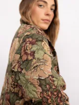 Campera tipo bomber con estampado floral estilo tapicería en tonos oscuros, con cuello clásico, cierre frontal con botones metálicos y bolsillos laterales.