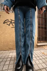 Pantalón de jean azul con cierre metálico en la parte inferior de la pierna.