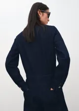 Mono largo de denim color azul oscuro, con cuello redondo, manga larga y cierre frontal de botones metálicos. Presenta corte recto y holgado en las piernas.