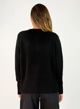 Sweater de punto color negro, con cuello redondo, manga larga y diseño con costura central vertical. Presenta un dobladillo acanalado en la cintura y puños, con un largo asimétrico siendo más corto en la parte delantera y más largo en la parte trasera.