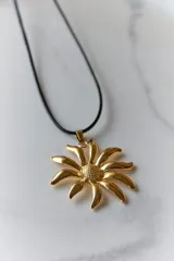 Collar con dije de acero quirúrgico en forma de flor tipo margarita, montado sobre un tiento de cuero negro.