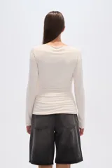 Top de manga larga ajustado al cuerpo, color beige claro, con escote bote y detalle de frunces drapeados en el torso.