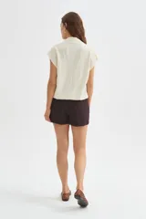 Blusa de poliéster color marfil, de corte holgado, sin mangas y con cuello buche drapeado.