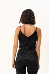 Top de satén negro con escote en V, decorado con detalles de encaje floral en el escote y en el ruedo. Presenta breteles finos ajustables y un corte asimétrico en la parte inferior.