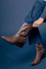 Bota de caña media color chocolate, confeccionada en cuero con textura granulada. Presenta una hilera de tachas metálicas doradas a lo largo del lateral y un taco cuadrado de altura media.