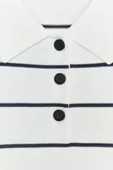 Jersey de punto blanco con rayas horizontales negras, cuello polo blanco y manga corta. Presenta una botonera frontal de tres botones negros.