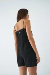 Monoprenda corta de color verde oliva, con tirantes finos ajustables, cierre frontal con botones y cintura elástica con cordón ajustable. Cuenta con bolsillos laterales.