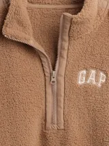 Buzo de polar tipo sherpa color marrón, con cuello alto y cierre frontal parcial. Presenta el logo de la marca bordado en el pecho y detalles de costuras reforzadas en hombros y mangas.