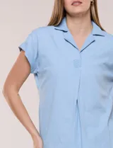 Blusa de diseño recto y textura suave de denim liviano color celeste, con cuello solapa abierto en V, pechera con detalle pespunteado y pliegue central. Presenta mangas cortas caídas con dobladillo fijo y ruedo ligeramente curvo.
