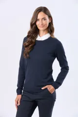 Buzo tejido en hilo de algodón color beige, con cuello redondo y manga larga. Presenta un corte clásico y un pequeño detalle metálico en la parte inferior izquierda.